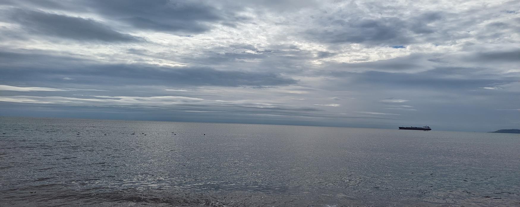 A view of the sea from the foreshore. The sky above has clouds which appear stormy.