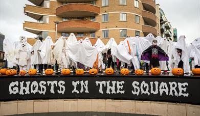 Picture showing a load of people dressed up a ghosts with lots of pumpkins above a sign saying Ghosts in the Square