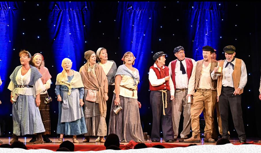 Picture of a group of people singing on stage dressed in sea shanty clothes