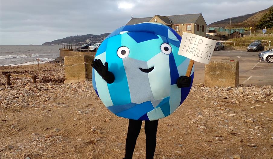 picture of a beach with a person dressed up with a sign say help the nurdles