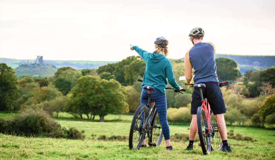 Image of a male and female on a bike in a field with trees around pointing at the landscape