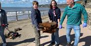 Picture taken beside the beach with 3 people carrying some rusty rubbish wearing gloves